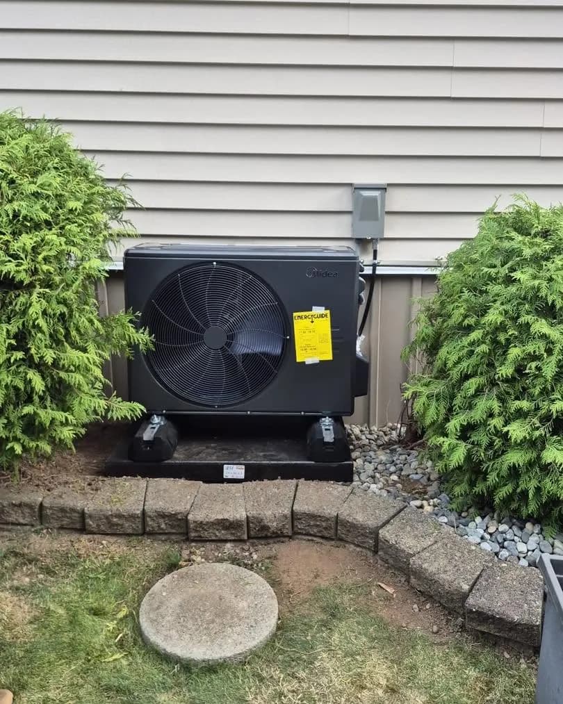 Finished heat pump install between cedar shrubs